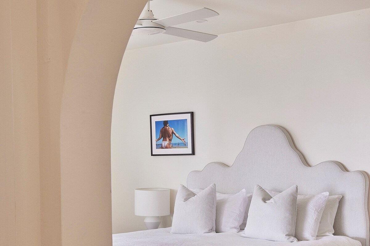 A bedroom with a large bed, a ceiling fan, a bedside lamp, and a framed picture on the wall.