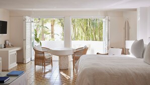 A hotel room with a bed, a desk, a chair, a table, and a large window with a view of palm trees. - Raes on Wategos  (Byron Bay)