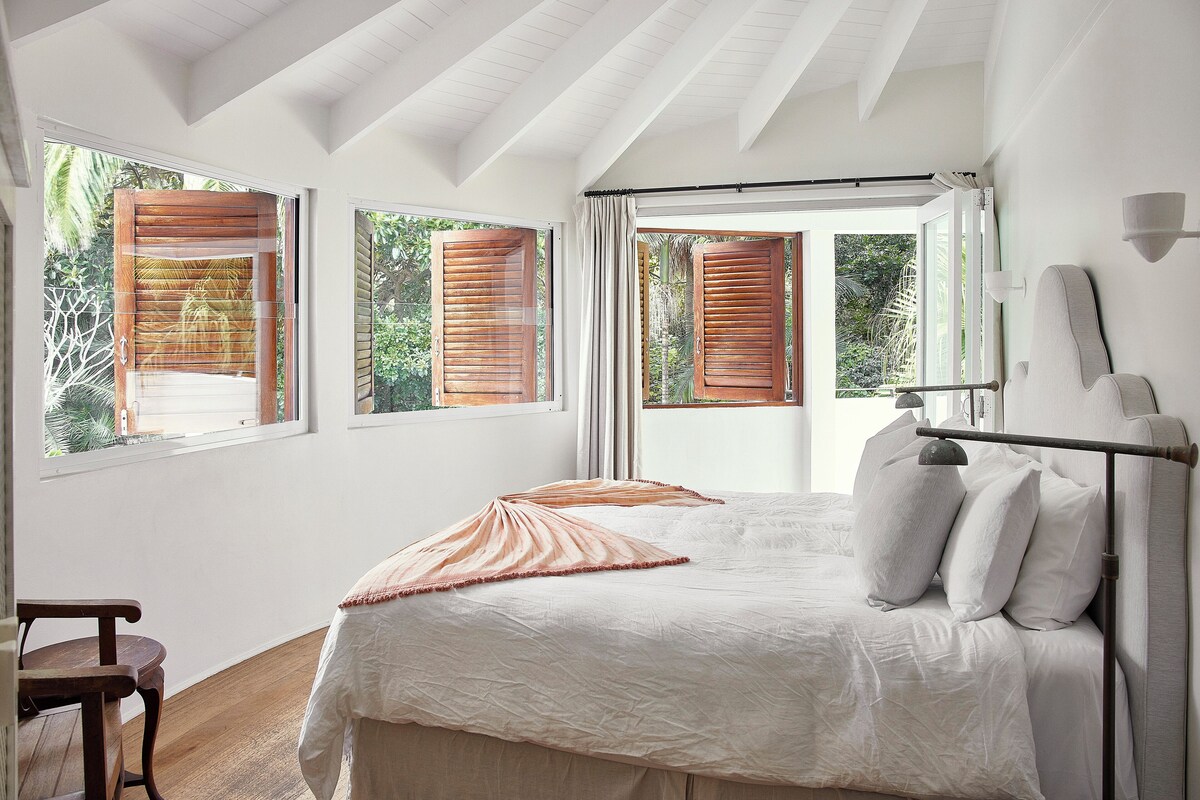 A bedroom with a bed, a chair, and a window with wooden shutters.
