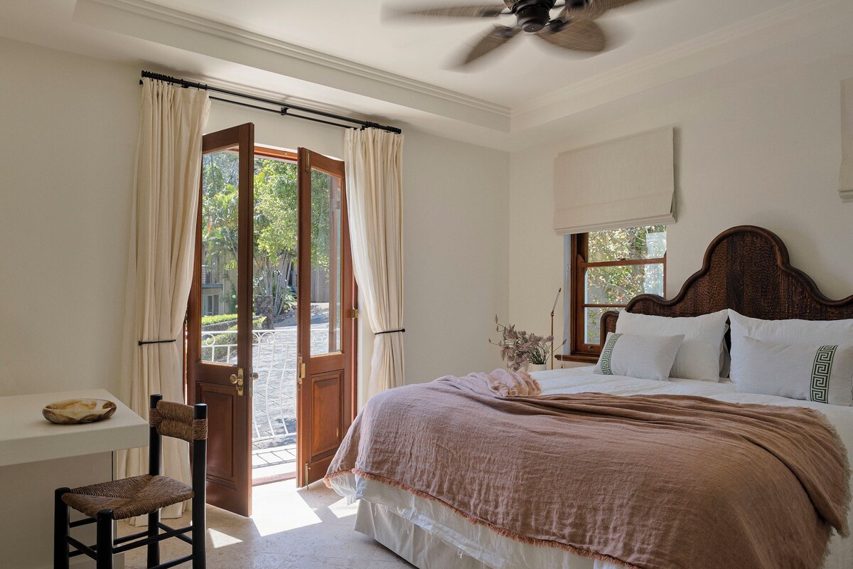 A bedroom with a bed, a ceiling fan, a window, and a door leading to an outdoor area.