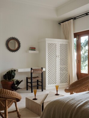 Ein Schlafzimmer mit Bett, Sessel, Kleiderschrank, Spiegel und einer Zimmerpflanze.