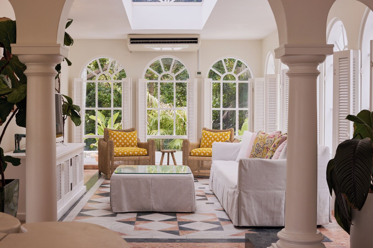 A sunlit room with a high ceiling, large windows, and a geometric patterned floor.