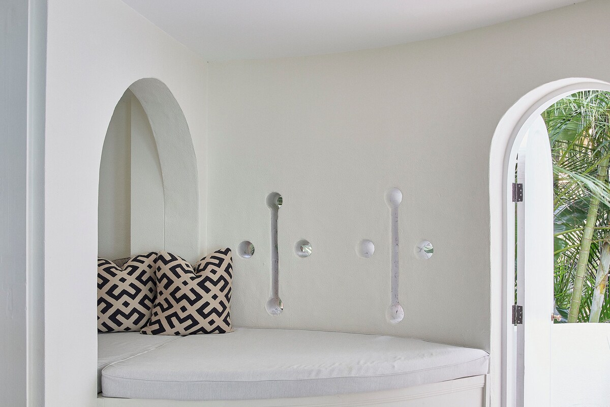 A corner seating area with a cushioned bench, a patterned pillow, and a door leading to an outdoor space.
