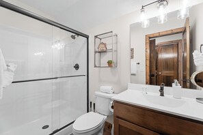 A modern bathroom with a glass shower enclosure, a toilet, a sink with a mirror, and a wooden vanity. - Tall Timbers Cabin, Private Hot Tub, Outdoor Pool, Free Daily Tickets & Near Thunder Ridge (Hollister)
