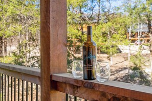 A wooden deck with a bottle of wine and two glasses on a railing. - Tall Timbers Cabin, Private Hot Tub, Outdoor Pool, Free Daily Tickets & Near Thunder Ridge (Hollister)