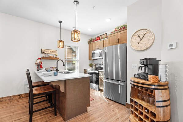 A modern kitchen with a central island, stainless steel appliances, pendant lighting, and a wine rack. - Tall Timbers Cabin, Private Hot Tub, Outdoor Pool, Free Daily Tickets & Near Thunder Ridge (Hollister)