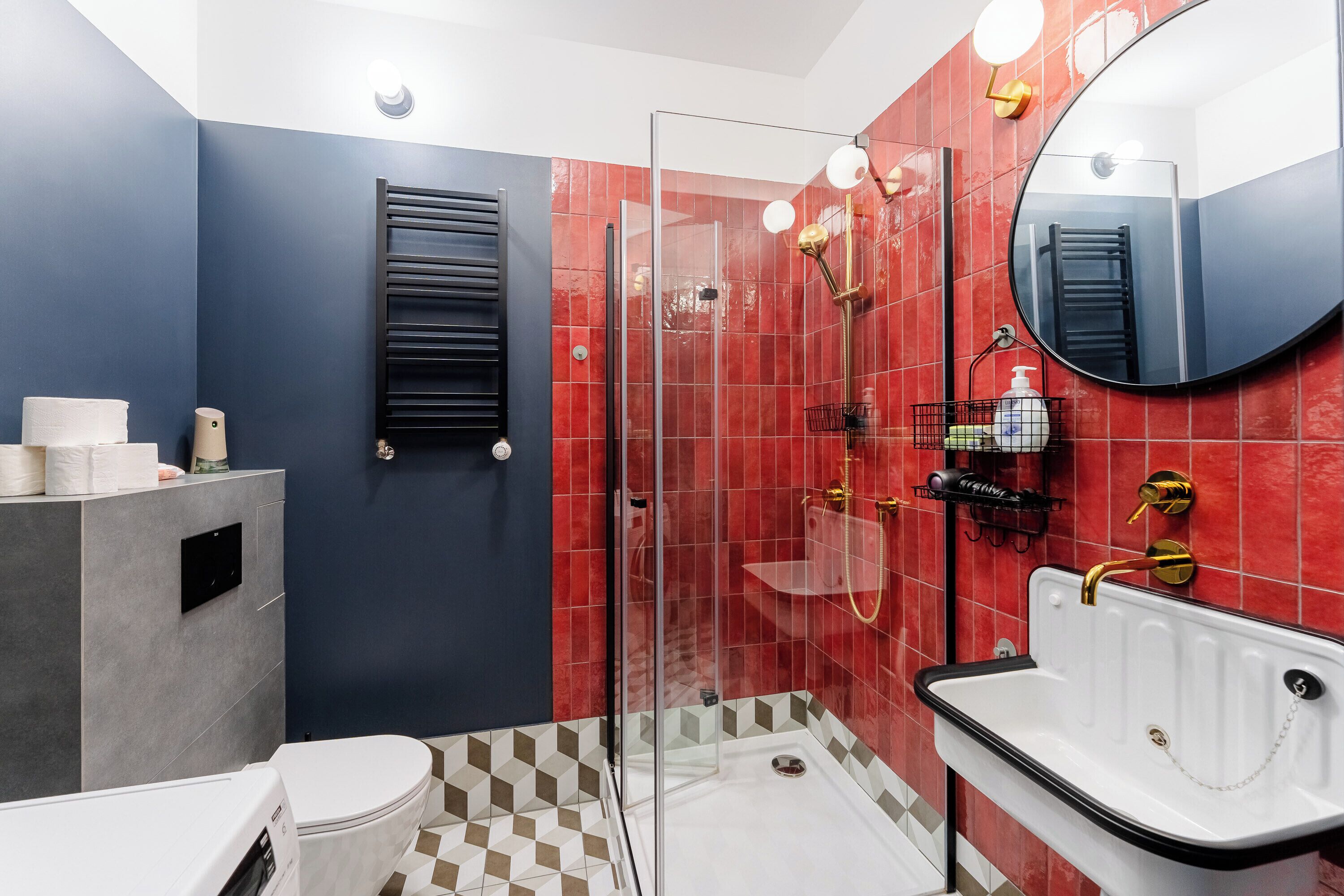 Une salle de bain moderne avec une douche à parois de verre, un lavabo blanc doté d’un robinet doré et un porte-serviettes noir.