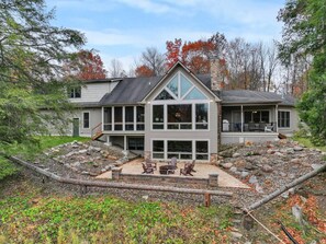 A two-story house with a stone foundation, large windows, and a covered patio with outdoor furniture. - Wine Country Waterfront • 100 Acres • Sleeps 16 (Jefferson)