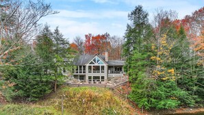 Une maison moderne dotée d’une grande terrasse, entourée d’une forêt dense et bordée par un plan d’eau.