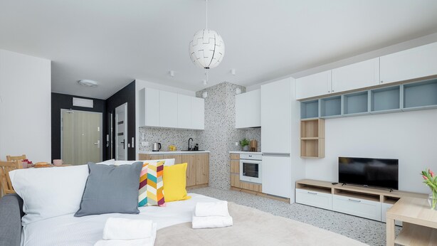 Una sala de estar moderna con sofá, televisión y zona de cocina con armarios y encimera.