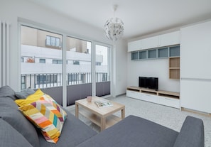Una sala de estar moderna con un sofá, una mesa de centro, un televisor y un balcón con vistas a edificios.