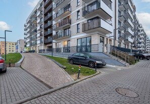 Moderni kerrostalo, jossa on useita parvekkeita, päällystetty kävelyreitti ja pysäköity auto.
