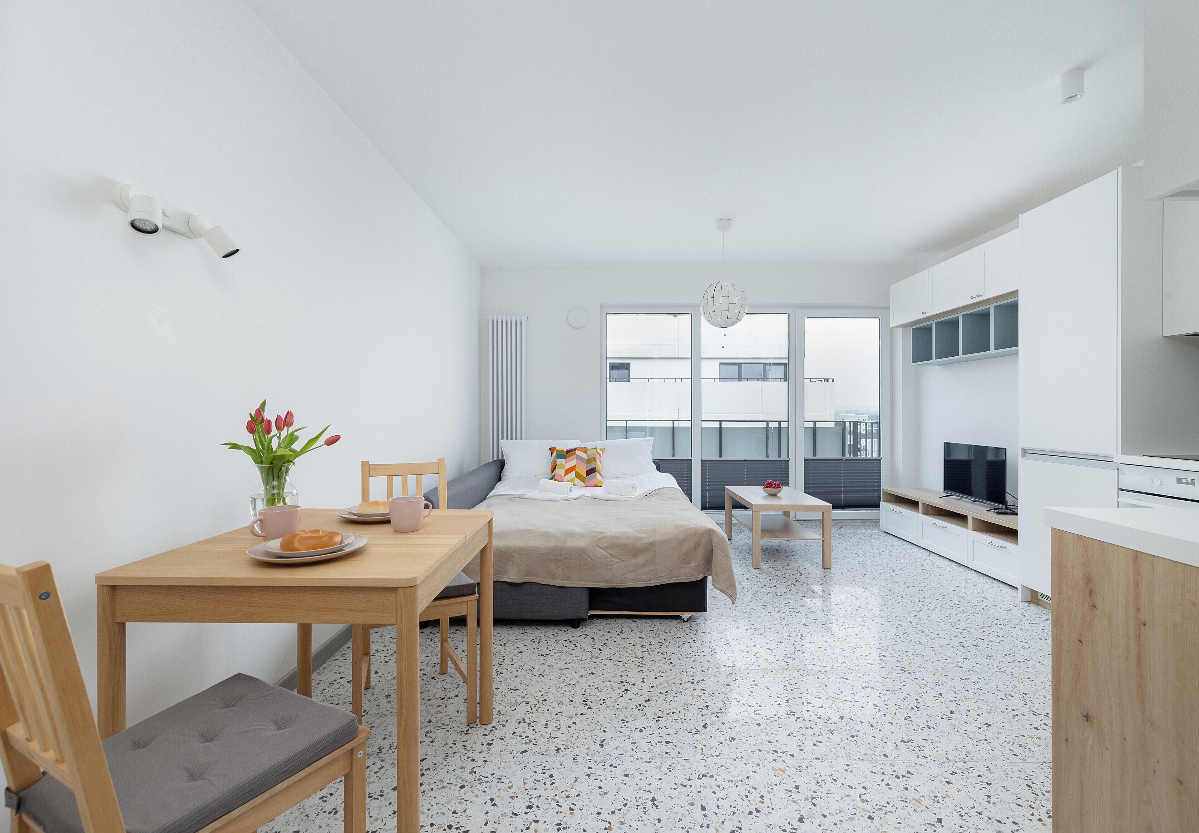A modern, minimalist bedroom with a bed, bedside table, and a window with a city view.