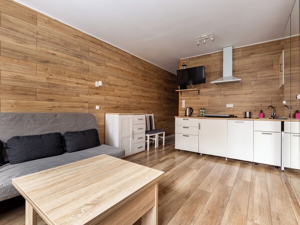 A modern kitchen with wooden cabinetry, a built-in stove, and a flat-screen TV mounted above the counter. - Głęboka Harmony Studio (Gdańsk)