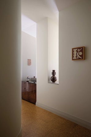 A hallway with a wooden cabinet, a vase, and a framed artwork on the wall.