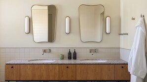 Une salle de bain avec deux lavabos, des meubles en bois et deux miroirs fixés au mur, chacun agrémenté d’une applique murale.