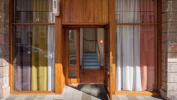 L’entrée d’un hôtel, avec une façade en bois, une enseigne indiquant « HÔTEL » et un escalier menant à l’intérieur.