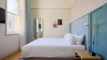 Habitación de hotel con cama, espejo, lámpara de pared, una mesita y ventana con cortinas.