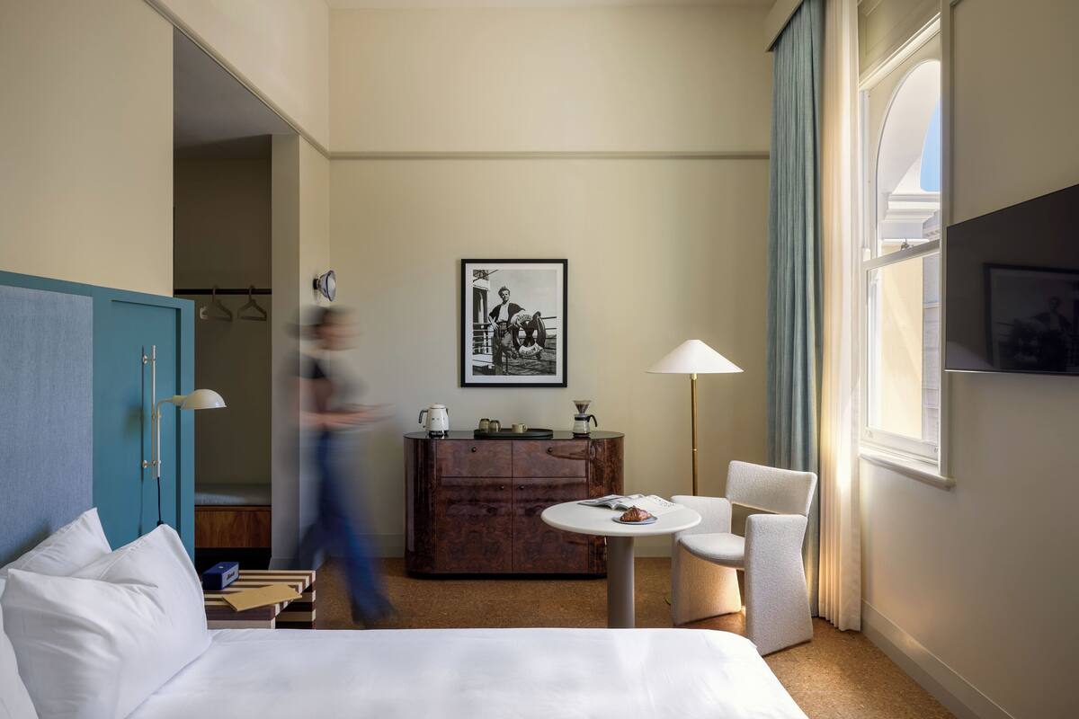 A hotel room with a bed, a desk, a chair, a dresser, and a window.