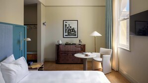 Une chambre d’hôtel avec un lit, un bureau, une chaise, une commode et un tableau encadré au mur.
