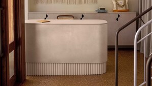 Une pièce avec une console blanche, une décoration murale en macramé et un escalier doté de rampes en métal.