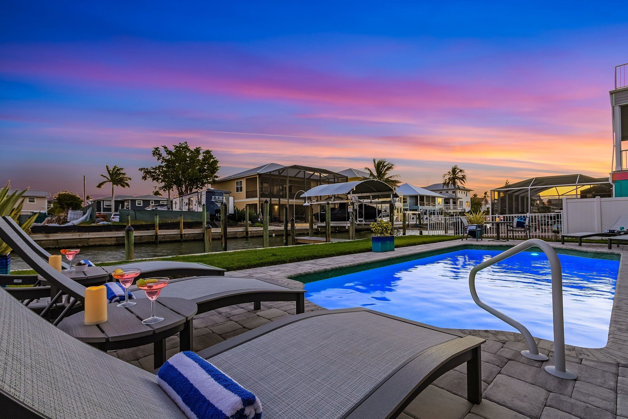 Un espace aménagé au bord de la piscine, avec des chaises longues, une piscine et une vue sur le coucher de soleil.