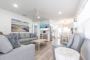 A modern living room with a grey sofa, a wooden coffee table, and a grey armchair. There is a television mounted on the wall and a ceiling fan. - Beach Escape on Siesta Key - Aloha Kai #7 - Roelens (Siesta Key)
