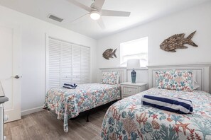 Ein Schlafzimmer mit zwei Betten, einem Deckenventilator, einem Fenster mit Jalousien und einem dekorativen Fisch an der Wand.