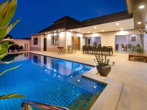 Una casa moderna con piscina, zona de comedor exterior y una planta grande en maceta.