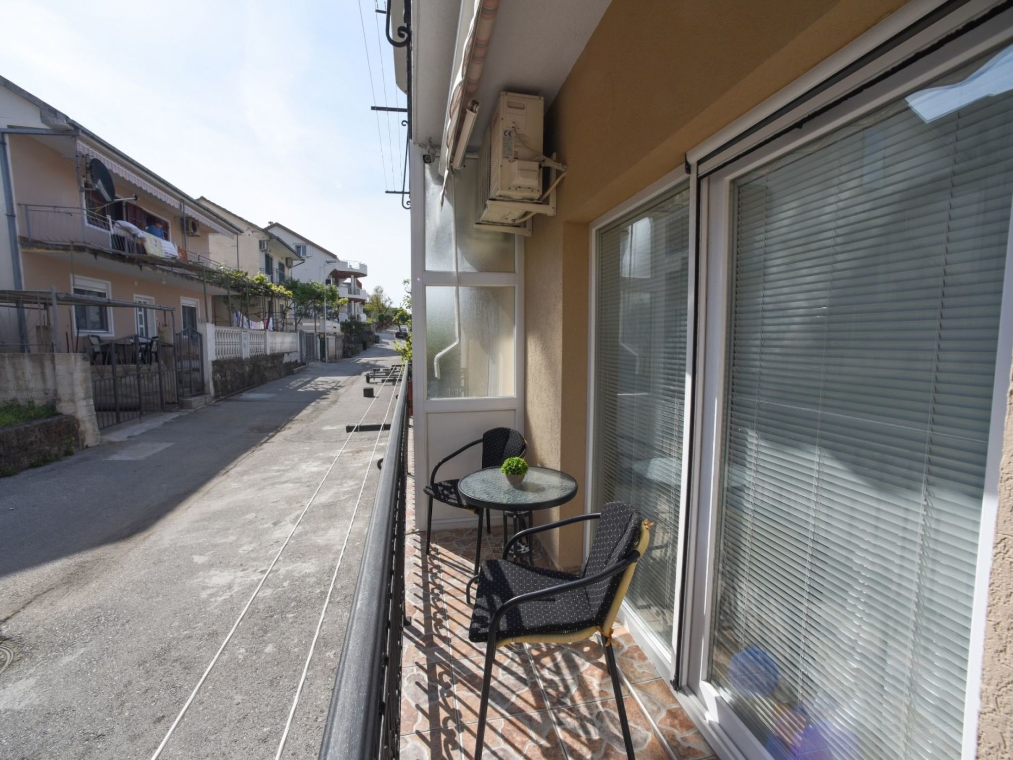 A balcony with a small table and chair, a sliding glass door, and a view of a residential street.