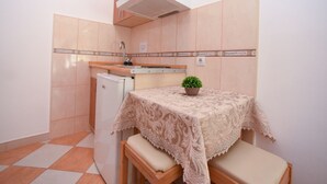Eine kleine Küche mit Spüle, einem Kühlschrank, einem Tisch mit Spitzenbettwäsche und einer Topfpflanze.