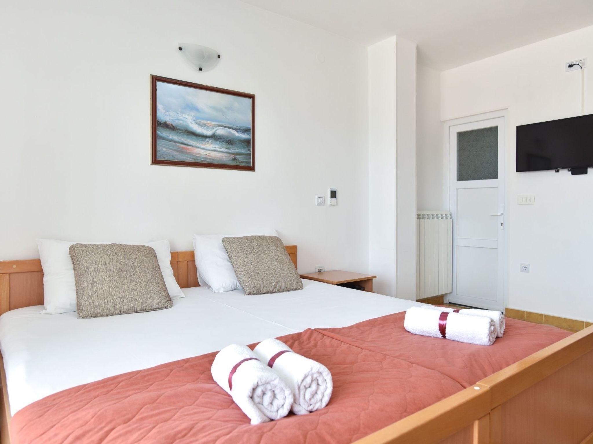 A hotel room with a bed, a painting on the wall, a bedside table, and a wardrobe.