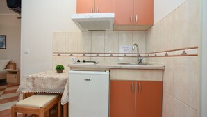 A compact kitchen with a sink, a small refrigerator, and a dining area with a table and bench. - Studio für 3 Personen by Interhome (Tivat)