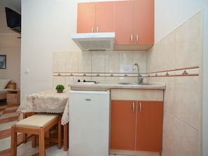 A compact kitchen with a sink, a small refrigerator, and a dining area with a table and bench. - Studio für 3 Personen by Interhome (Tivat)