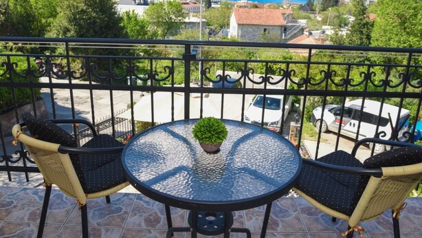 A balcony with a round glass table and two wicker chairs, overlooking a scenic view of a town and mountains. - Studio für 3 Personen by Interhome (Tivat)