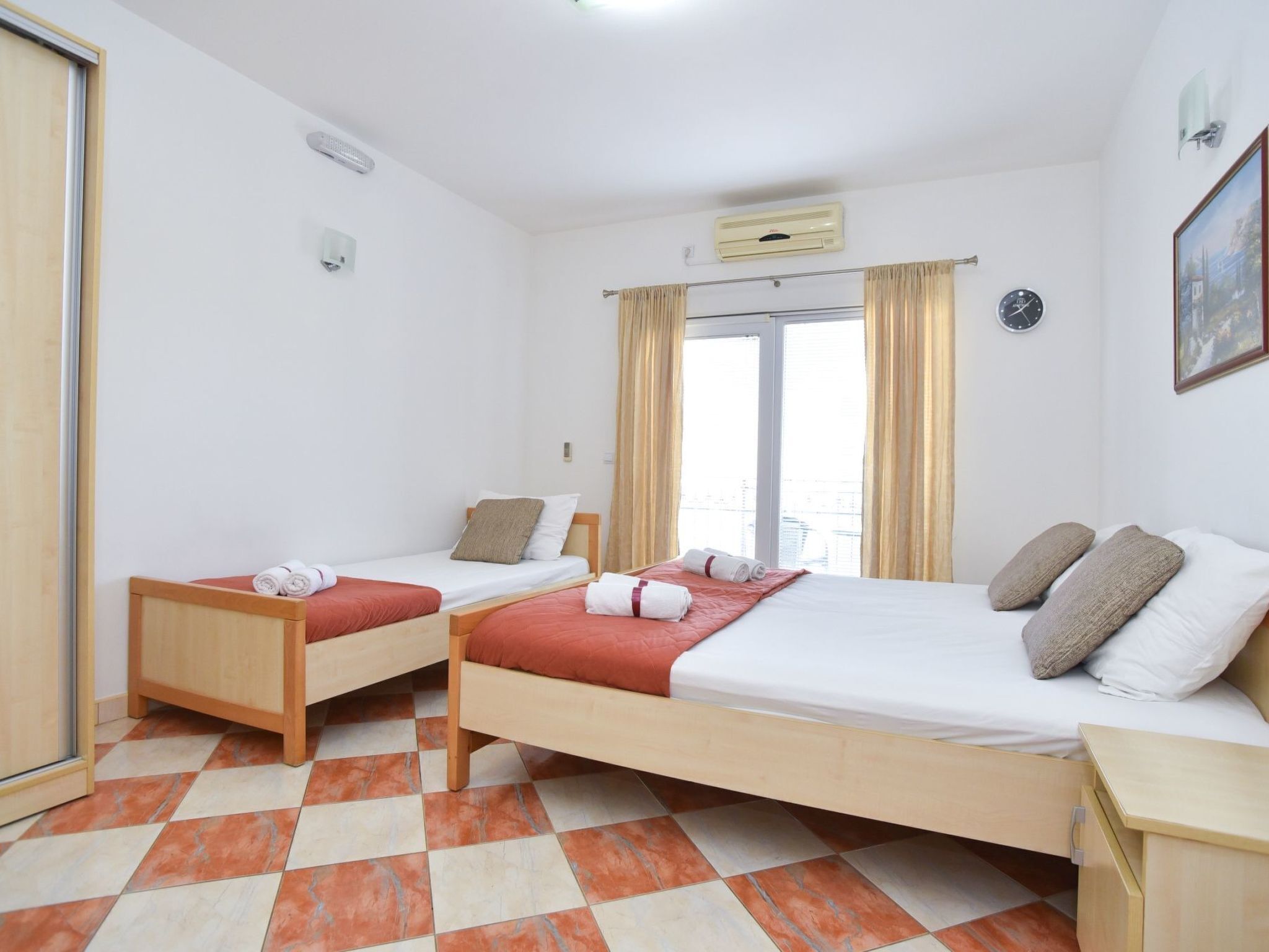 Habitació d'hotel amb dos llits individuals, una finestra gran amb cortines, un rellotge a la paret i un terra amb rajoles.