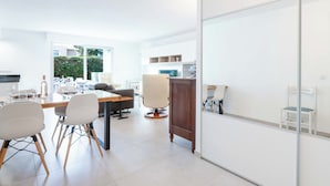 Eine moderne Küche mit weißen Schränken, ein Essbereich mit Tisch und Stühlen und Blick auf Grünfläche.