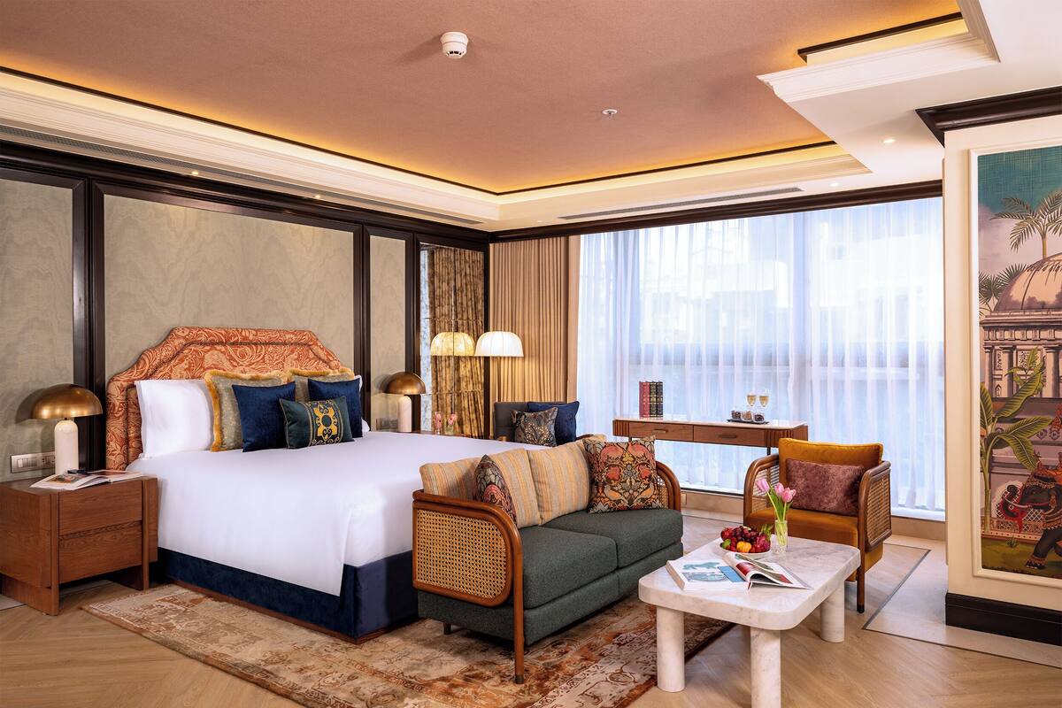 A hotel room with a large bed, a sofa, a coffee table, a desk, and a window with curtains.