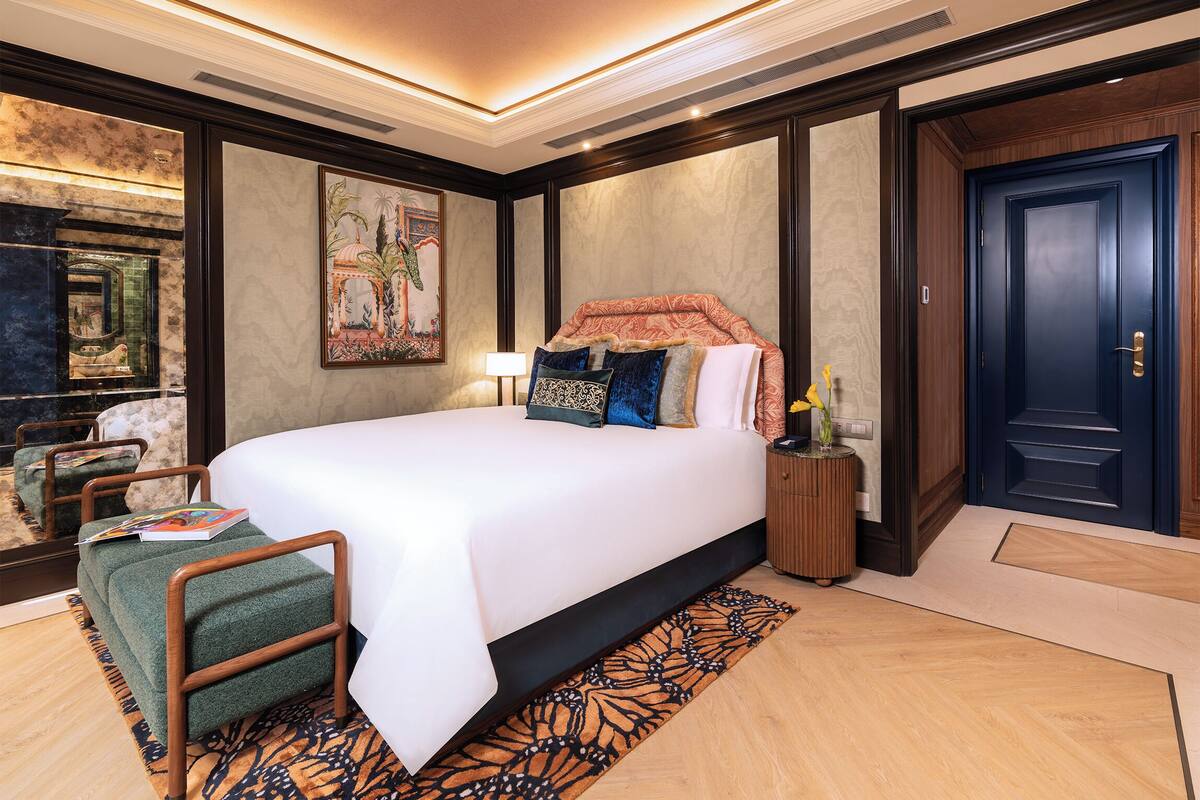 A hotel room with a large bed, a nightstand, a chair, a mirror, and a door.