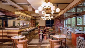 Un restaurante con zona de bar, mesas redondas y sillas, y grandes ventanales que ofrecen vistas.