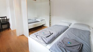 Un dormitorio con dos camas, vigas de madera en el techo, una silla y un armario blanco.