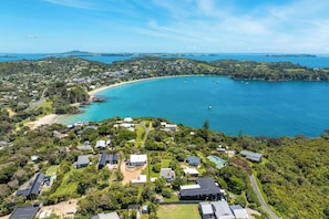 Vista aérea de uma área residencial costeira, com casas, uma praia e uma baía com barcos.