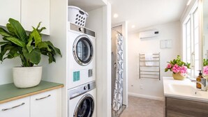 A laundry room with a front-loading washer and dryer, a potted plant, and a shower area with a patterned curtain.