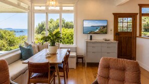 A dining area with a wooden table, chairs, a potted plant, and a view of the ocean through large windows.