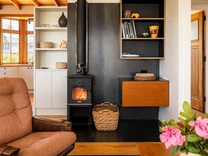 A cozy living room with a modern fireplace, a comfortable sofa, and a bookshelf. - Pat's Bach - Elevated Bay Views Over Little Oneroa (Waiheke Island)