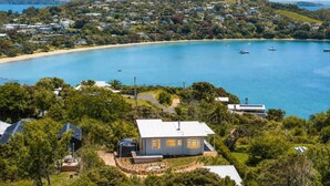 A coastal property with a large house surrounded by lush greenery, a sandy beach, and a clear blue sea with boats.