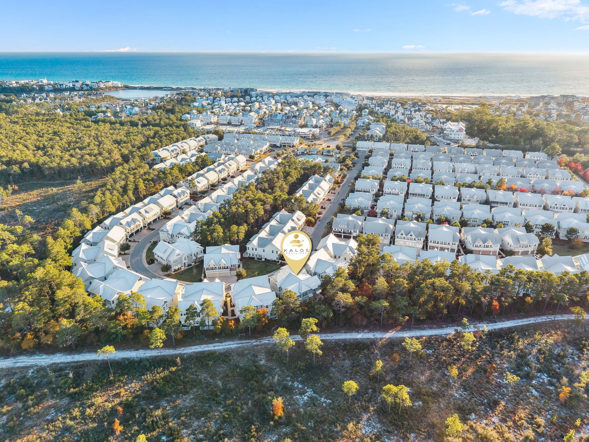 Ein Luftbild eines Küstenresorts mit kreisförmiger Anordnung von Villen, einem zentralen Platz und einem Strand im Hintergrund.