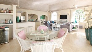 Uma sala de estar espaçosa com uma mesa de jantar de vidro, cadeiras de vime, um sofá e uma televisão.