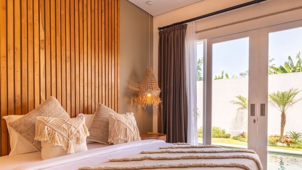A bedroom with a bed, pillows, a hanging light fixture, and a view of the outdoors. - Haus Moana by Interhome (Seminyak)