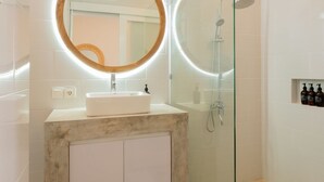 A modern bathroom with a round mirror, a rectangular sink, and a glass-enclosed shower area. - Haus Moana by Interhome (Seminyak)